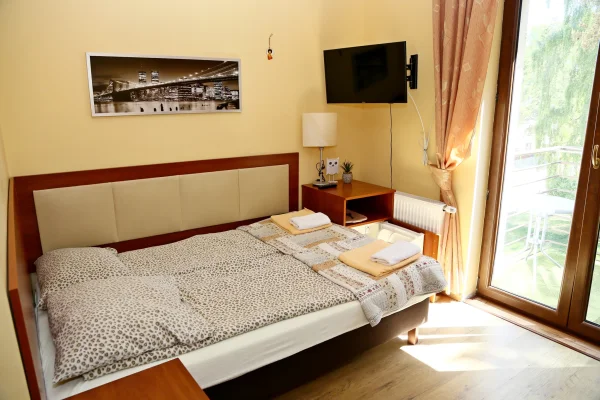 Podwójne łóżko w paisley, czarno-biały plakat z nocnym Nowym Jorkiem, telewizor na ścianie i balkon z białym stolikiem.
