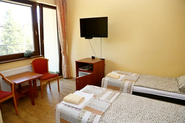 Wnętrze pokoju w pensjonacie w Pobierowie — dwa łóżka z patchworkowymi narzutami, telewizor i szafka z lodówką.
