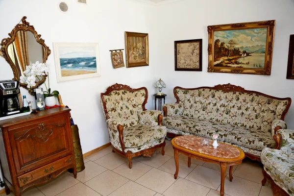 Klasyczny salon z rzeźbioną sofą w kwiatowej tapicerce, owalnym stolikiem z różowym blatem, obrazami i złotym lustrem.